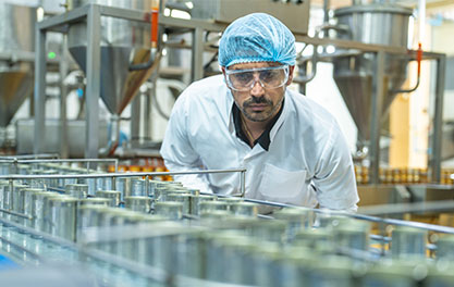 Person in Schutzkleidung &uuml;berwacht Produktionslinie mit Beh&auml;ltern