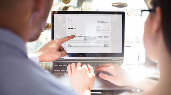 Zwei Personen betrachten Invoice auf Laptop, eine zeigt auf Bildschirm