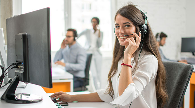 Frau mit Kopfh&ouml;rer l&auml;chelt am Schreibtisch beim Telefonieren im B&uuml;ro