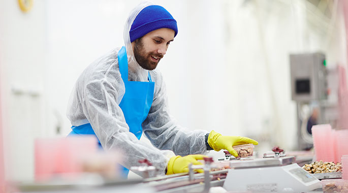 Mann in Schutzkleidung arbeitet an Produktionslinie mit Lebensmitteln