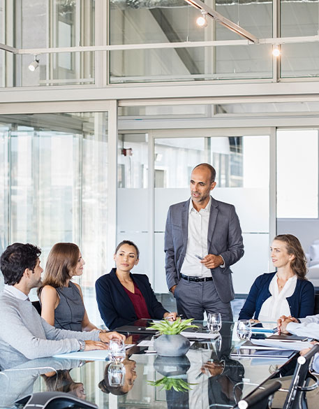 Personen sitzen um Konferenztisch w&auml;hrend eine Person spricht in hellem B&uuml;ro
