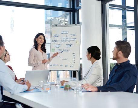 Frau pr&auml;sentiert Marktstrategie am Whiteboard vor Zuh&ouml;rern am Tisch