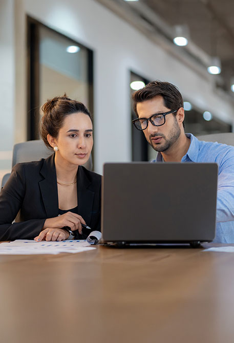 Zwei Personen schauen gemeinsam auf Laptop mit Unterlagen im Gro&szlig;raumb&uuml;ro 
