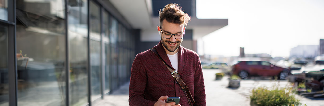 Mann steht vor einem Geb&auml;ude und l&auml;chelt w&auml;hrend er auf sein Handy schaut