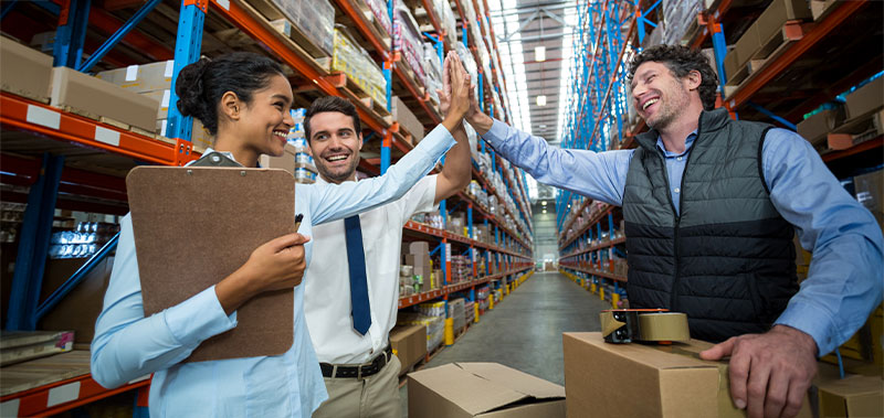 Drei Personen im Lager geben sich ein High-Five zwischen Regalen