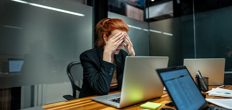 Frau sitzt ersch&ouml;pft vor einem Laptop und h&auml;lt den Kopf in den H&auml;nden