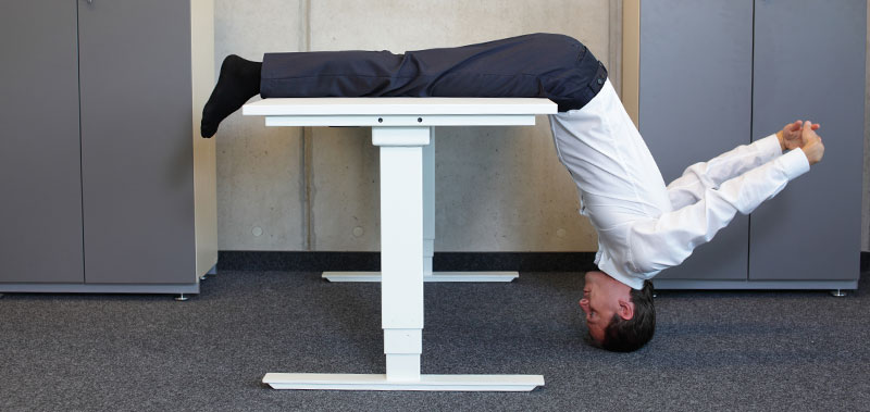 Mann liegt kopf&uuml;ber auf einem Schreibtisch in ungew&ouml;hnlicher Position
