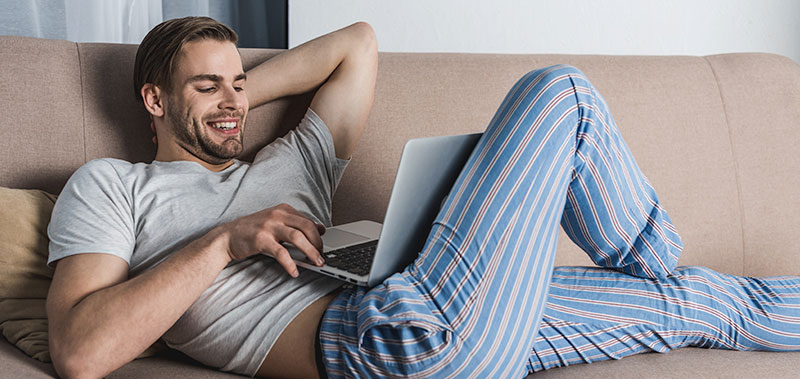 Mann liegt entspannt auf dem Sofa und nutzt einen Laptop